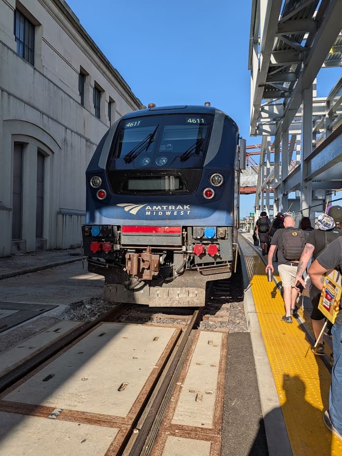 An Amtrak Midwest locomotive numbered 4611 standing at a sunlit platform at Kansas City Union Station, with attendees walking along the platform toward the cars