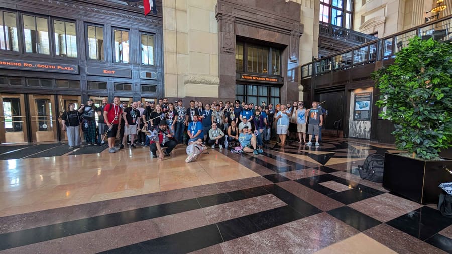 The full Hobocon 2 group posed together on the polished marble floor of the Grand Hall at Kansas City Union Station, under the arched windows and the Union Station Stories sign, some holding antennas and telescoping poles