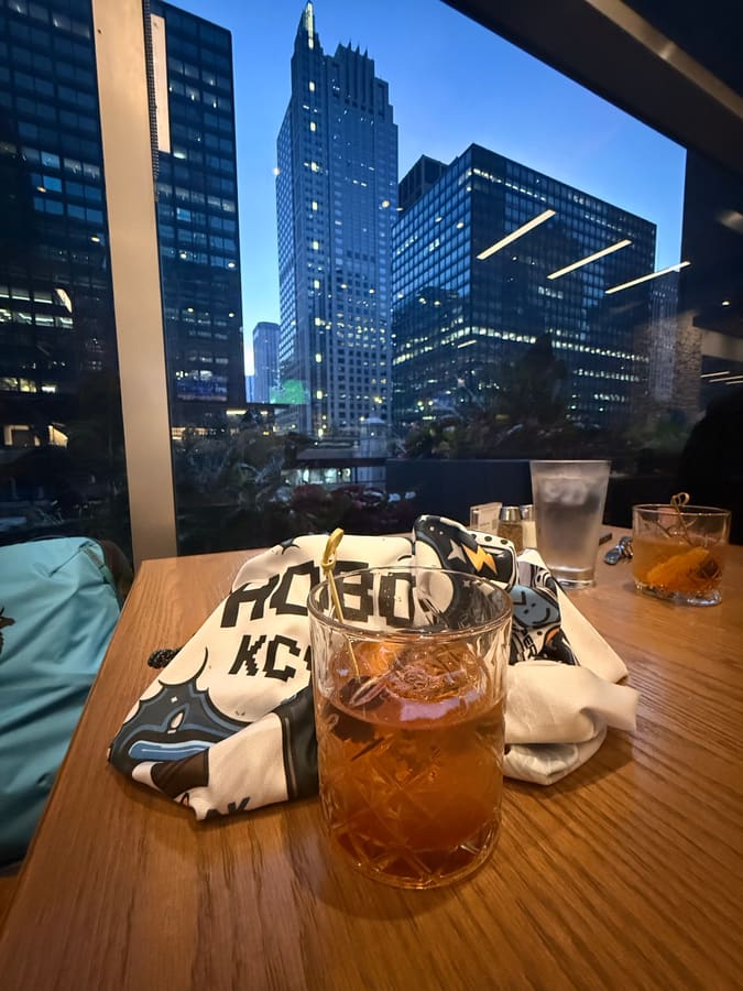 An old fashioned in a cut-glass tumbler on a restaurant table, with floodlit downtown Chicago high-rises filling the window behind